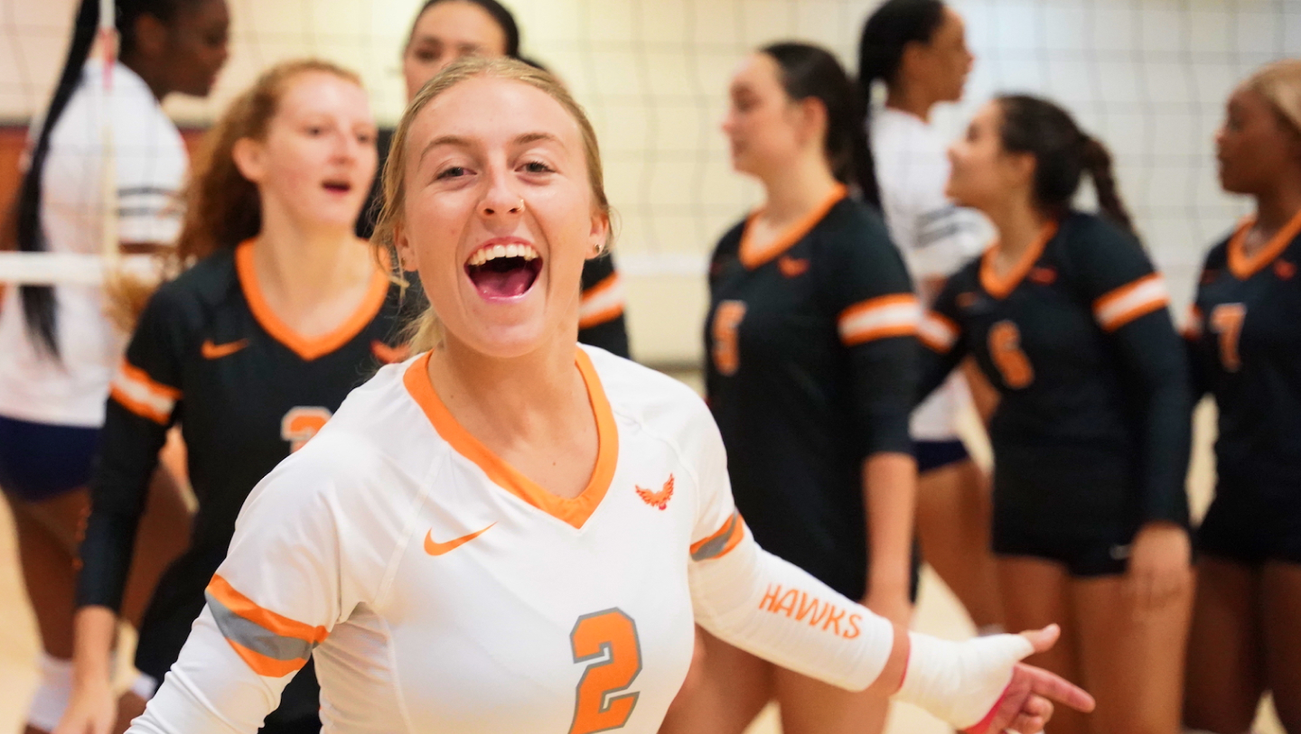 A smiling female volleyball player in foreground with other players in the background