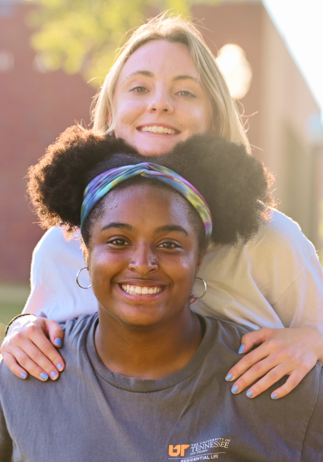 Two students, one giving a piggy back ride, smiling