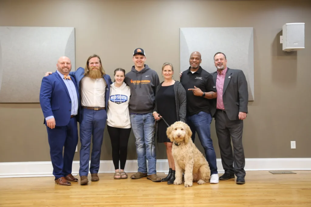 Folks posing for a photo in a lecture hall, dog at the front