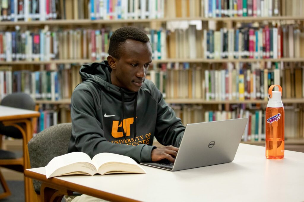 A student in UTS sweatshirt in the library, working on his laptop