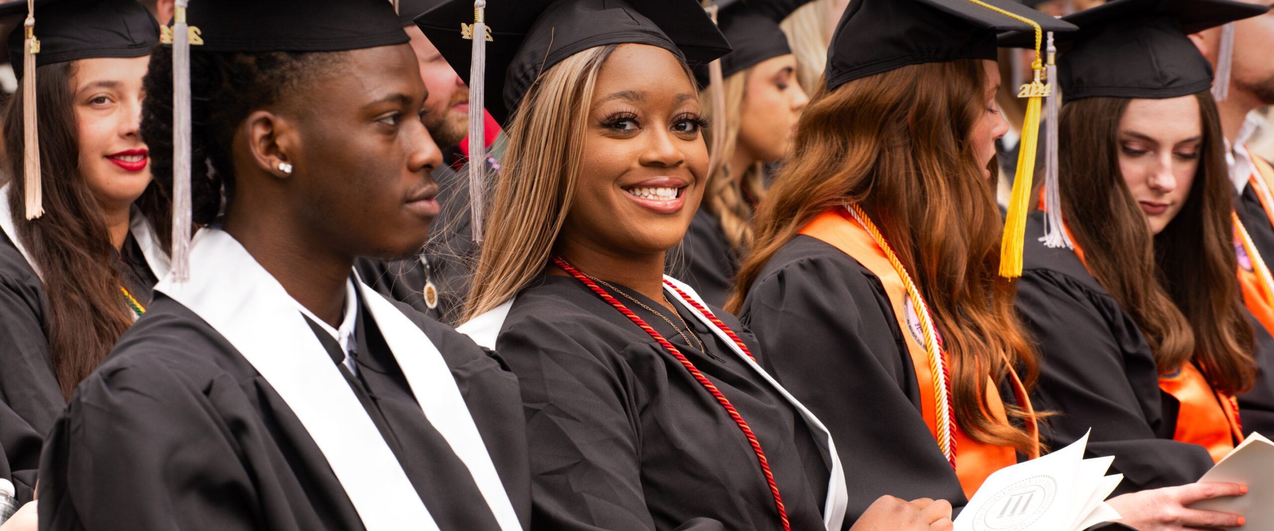 Several graduates in cap and gown, with one looking at camera and smiling