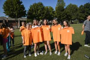 A group of students holding up their orange Into the Streets service tshirts while standing on the green.
