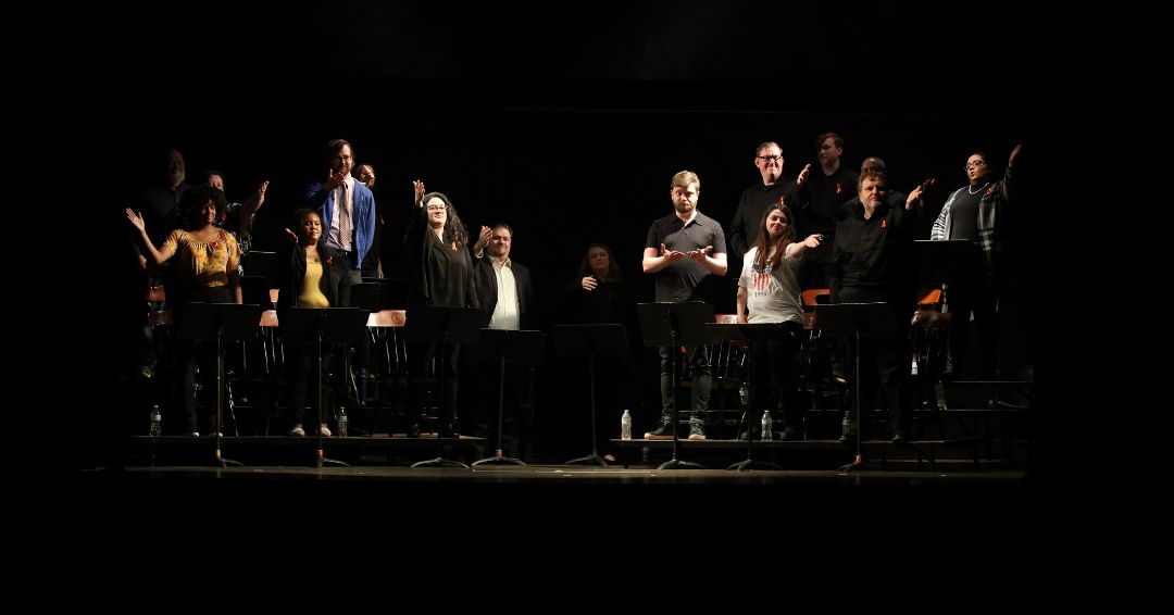 Performers on stage with hands raised on a darken stage.