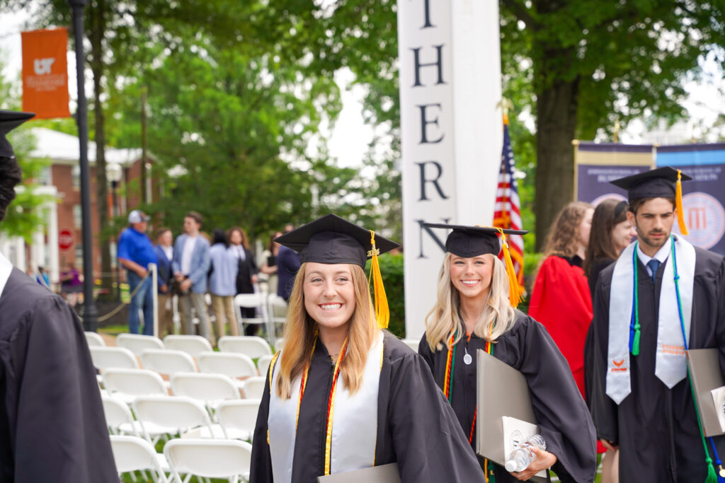 Students in a line smiling while wearing cap and gown at graduation ceremony